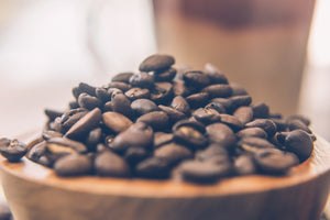 Fresh Roasted Coffee Beans in wooden bowl.  Medium to dark roast rich in flavor with coffee mug out of focus in background